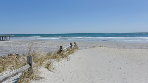 Ein Sandstrand mit einer Holzbank und einem Zaun.