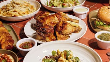 Variedad de platos, incluyendo pollo a la parrilla, pasta y una hamburguesa, sobre una mesa.
