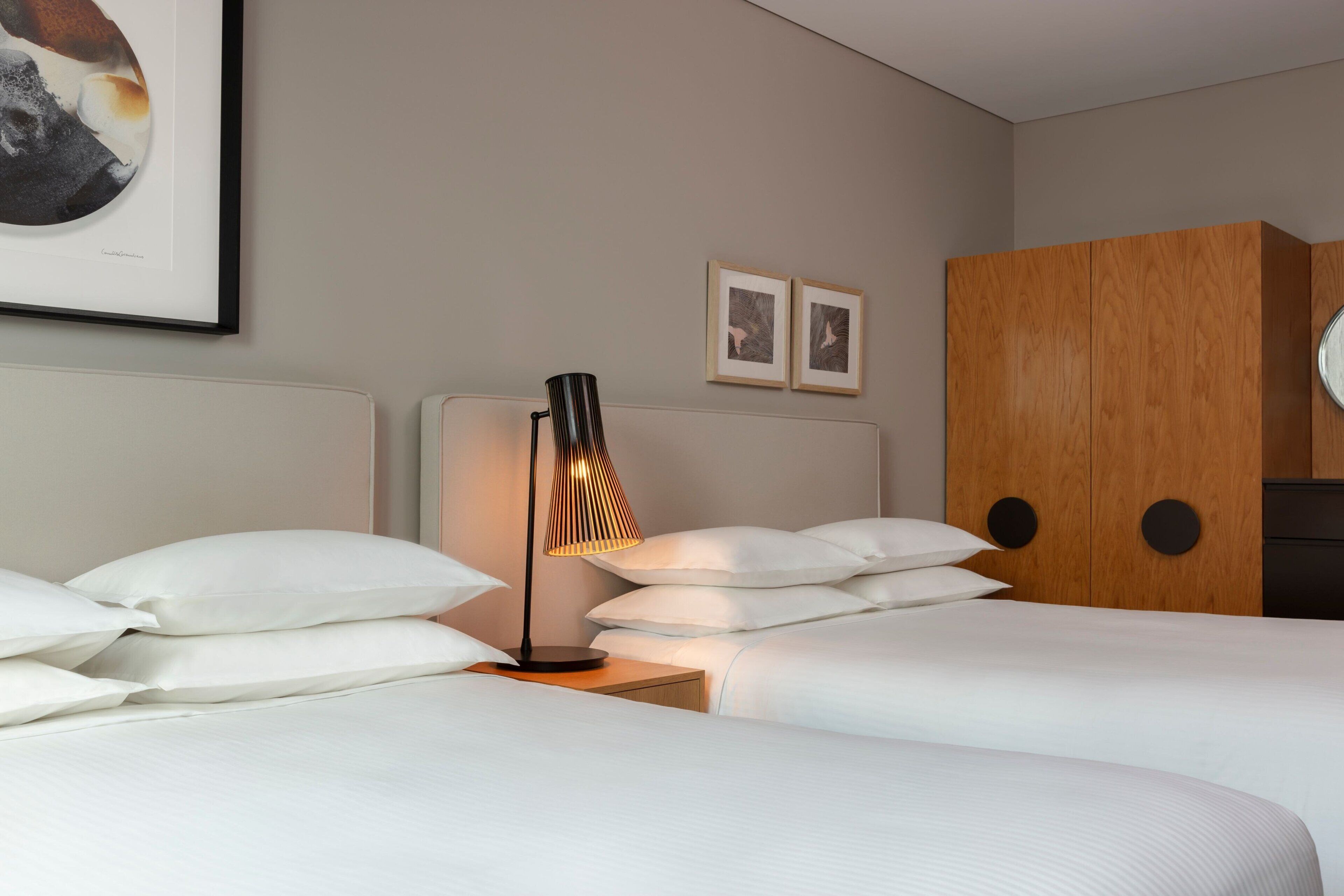 Ein Hotelzimmer mit zwei Betten, einem Nachttisch mit Lampe und einem Holzschrank.