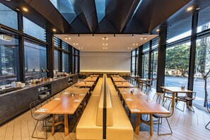 A modern dining area with long wooden tables and benches, large windows, and a view of the street. - Four Points By Sheraton Sydney, Central Park (Chippendale)