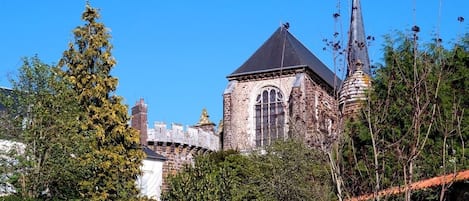 Un bâtiment historique doté d’une tour imposante et de fenêtres en arc de cercle, entouré d’une végétation luxuriante.