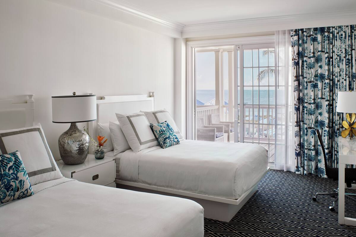 Een hotelkamer met twee bedden, een groot raam met uitzicht op zee en een kamerbreed tapijt met dessin.