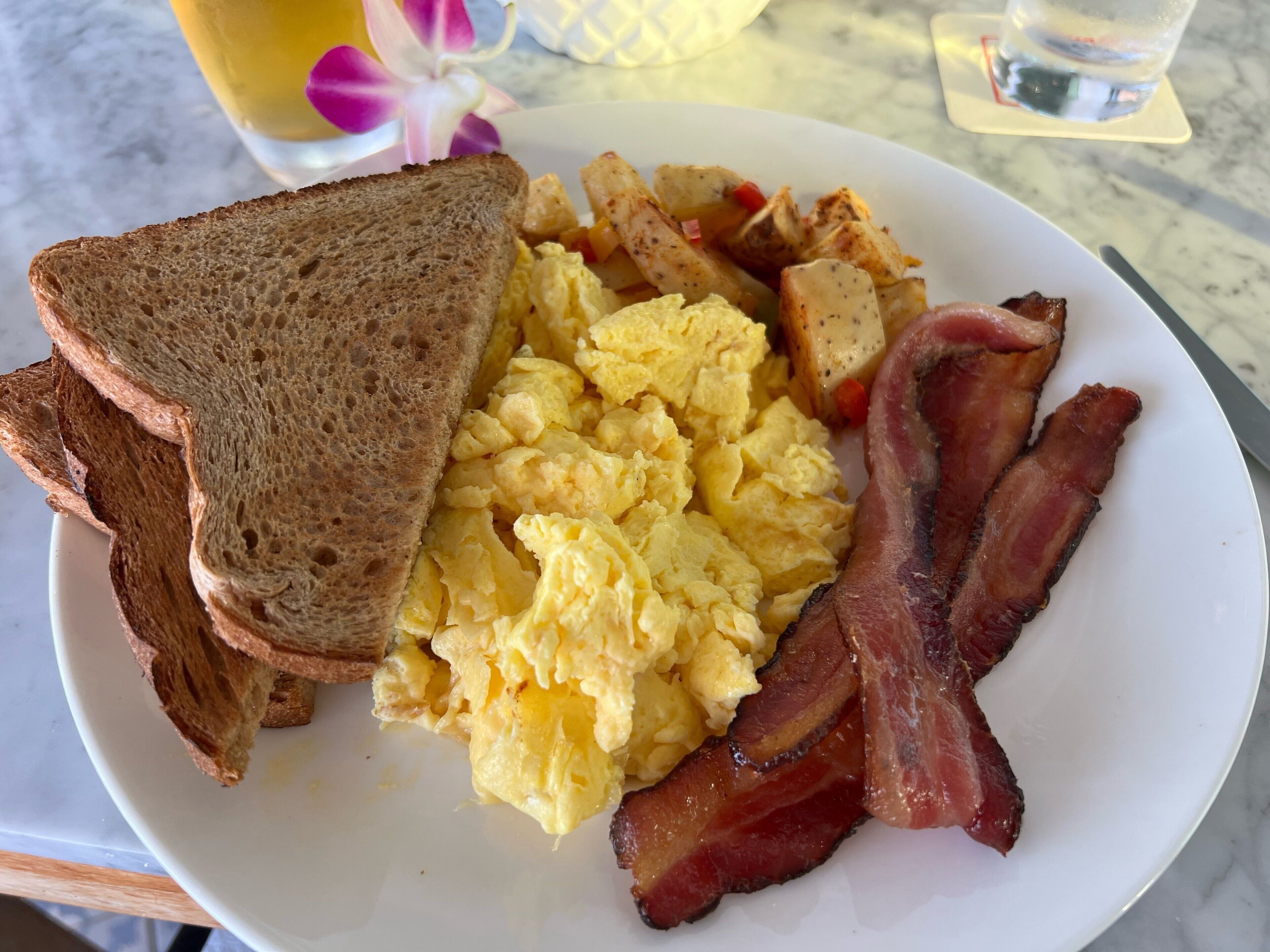 A plate with scrambled eggs, bacon, toast, and hash browns.