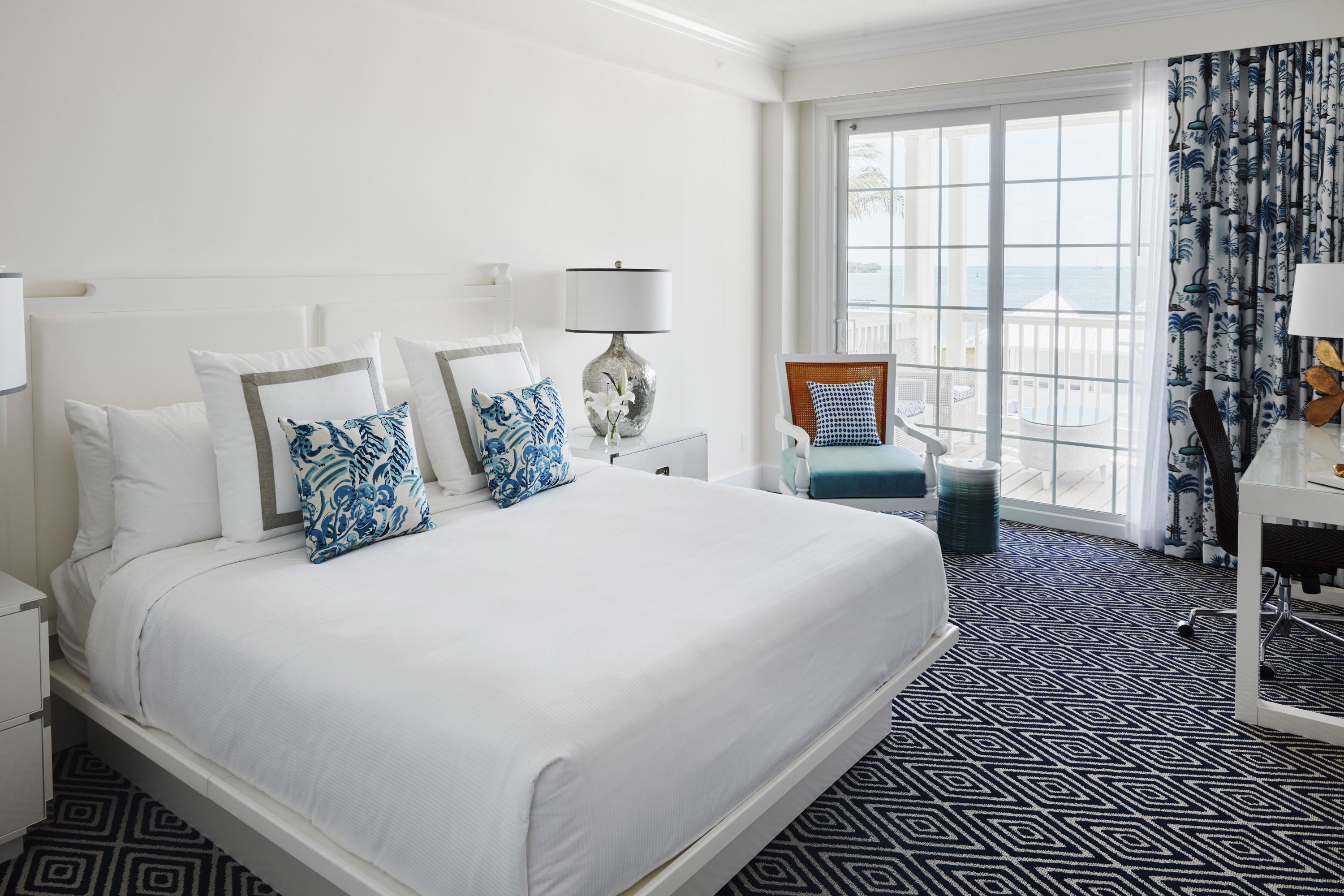 Habitación de hotel con una cama grande, una silla, un escritorio y vista al océano.