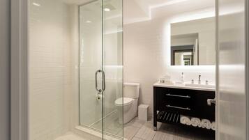 Un baño moderno con ducha envuelta en vidrio, azulejos blancos, un mueble de tocador negro con espejo y un inodoro blanco.