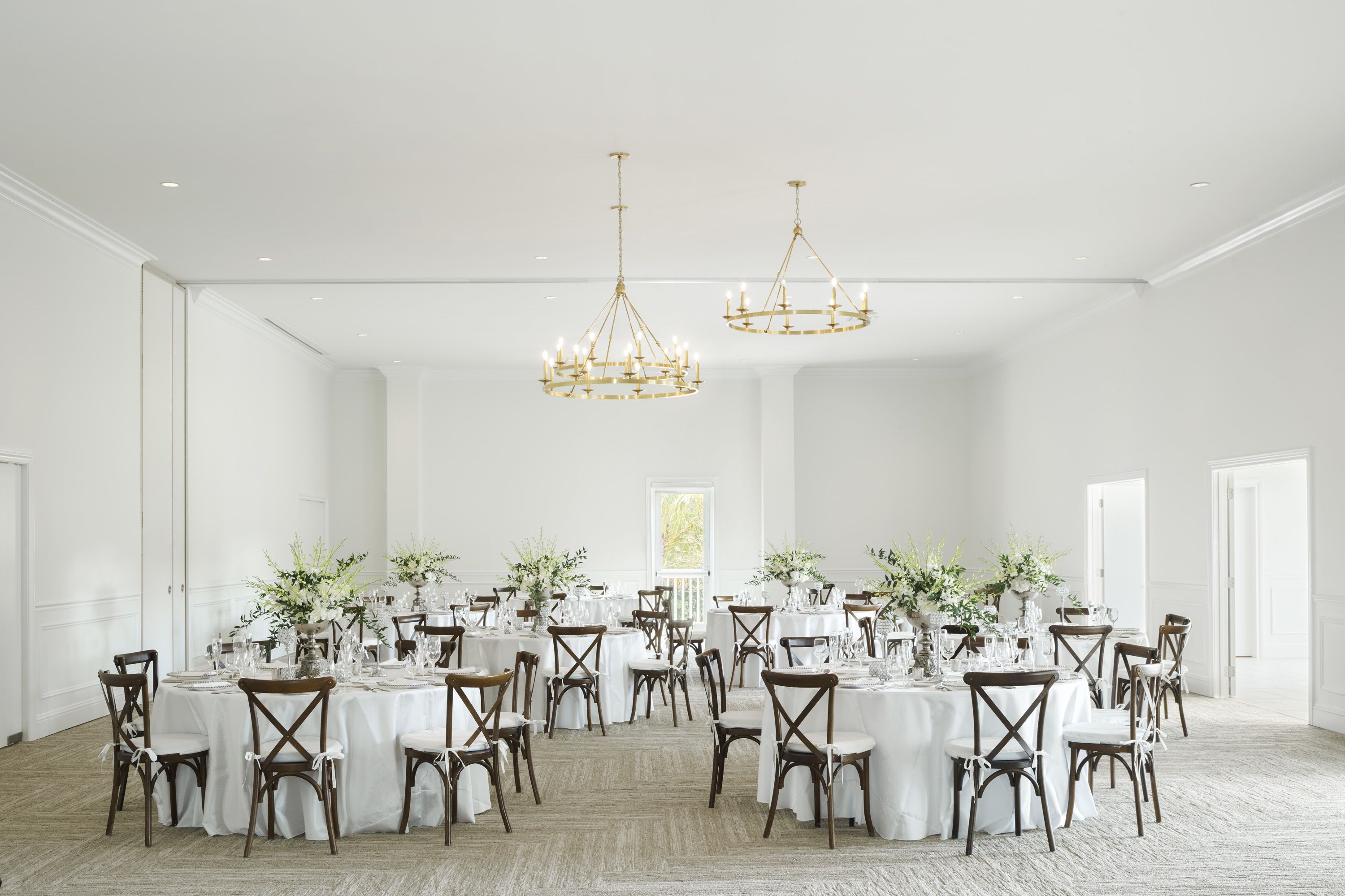 A spacious banquet hall with round tables, white walls, and chandeliers.