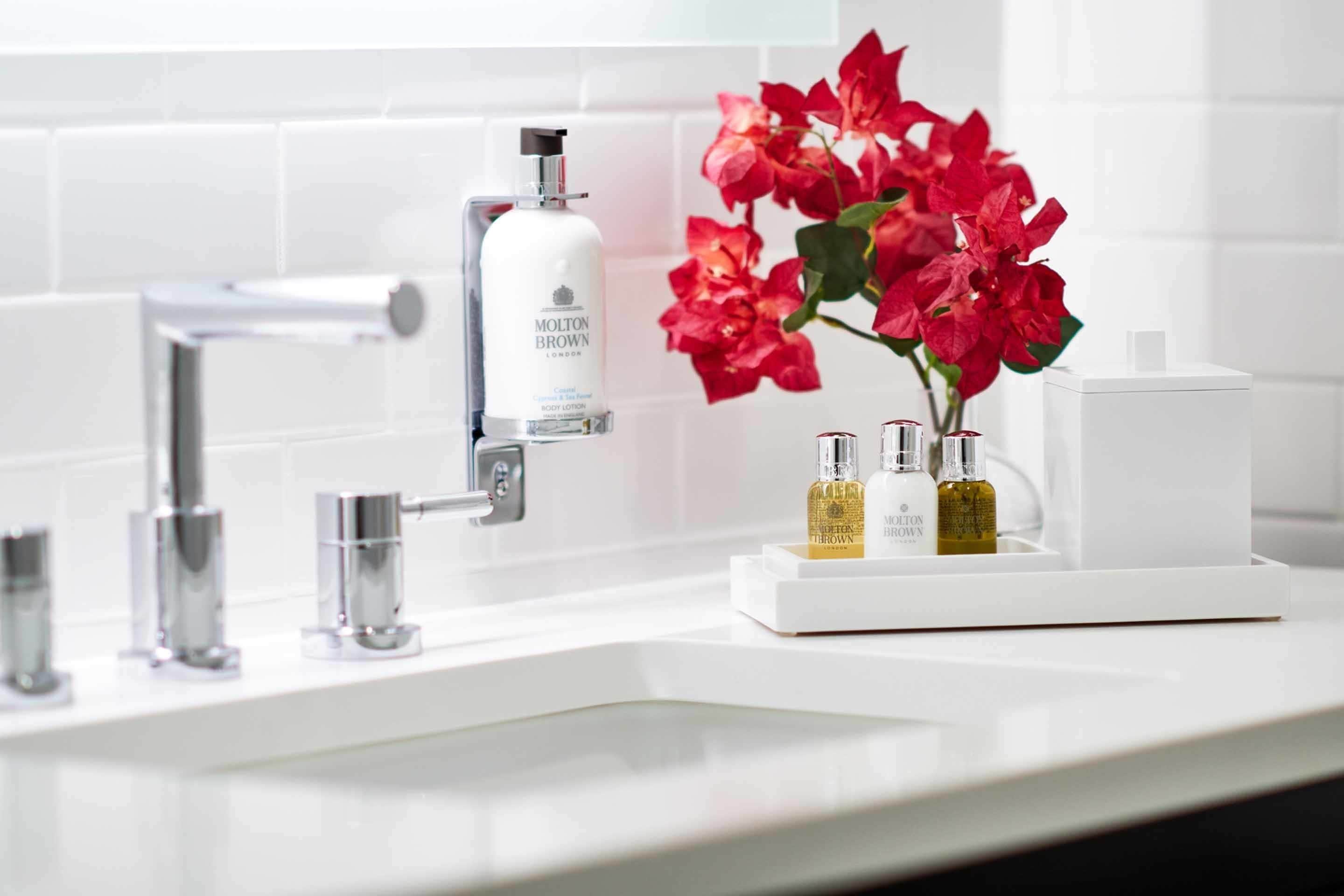 A modern bathroom with a white sink, chrome fixtures, and a floral arrangement.