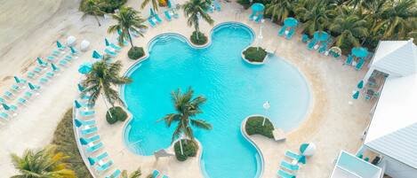 Vue aérienne d’un complexe hôtelier doté d’une piscine centrale, entourée de chaises longues et de palmiers.