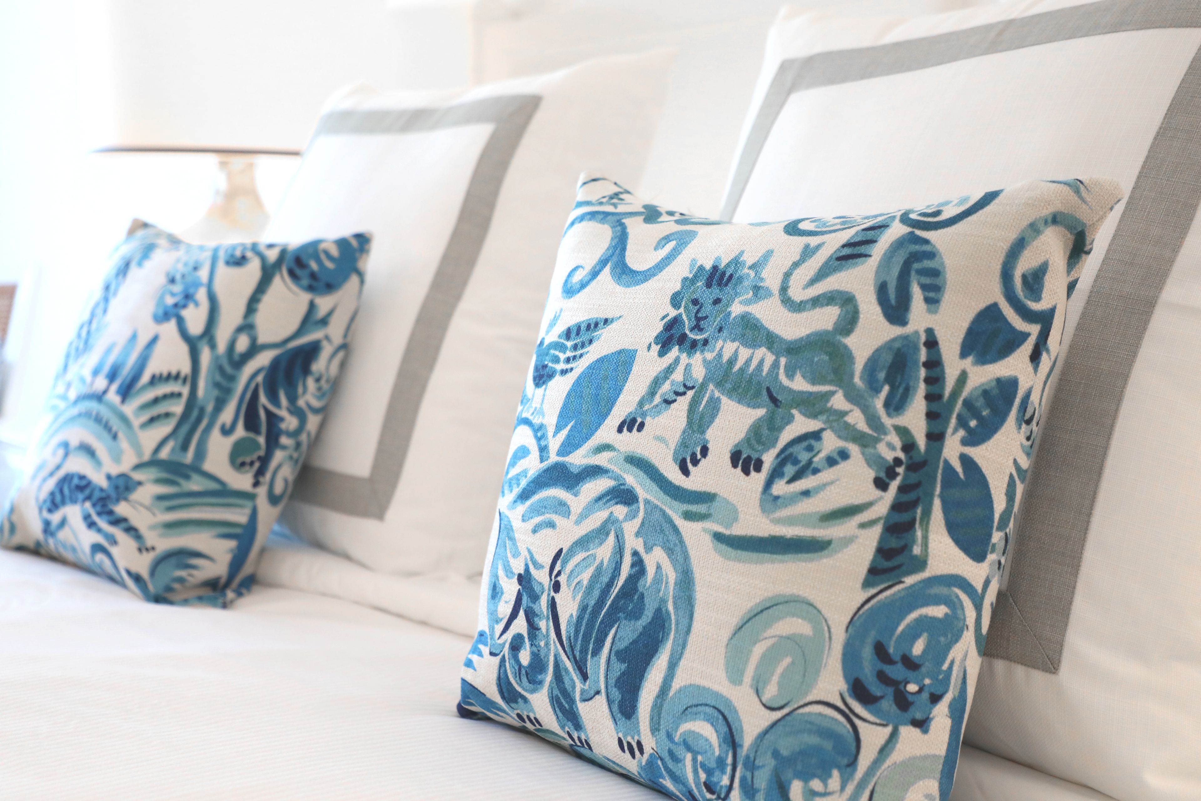A bed with white bedding and blue patterned pillows.