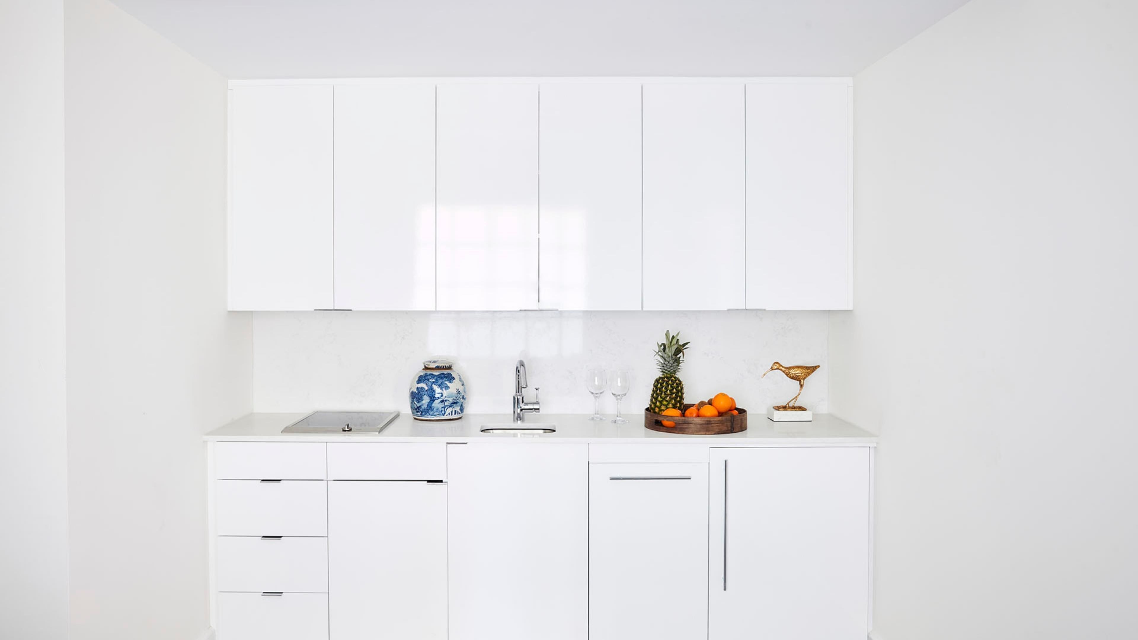 A modern kitchen with white cabinetry, a stainless steel sink, and a fruit bowl with oranges and a pineapple.
