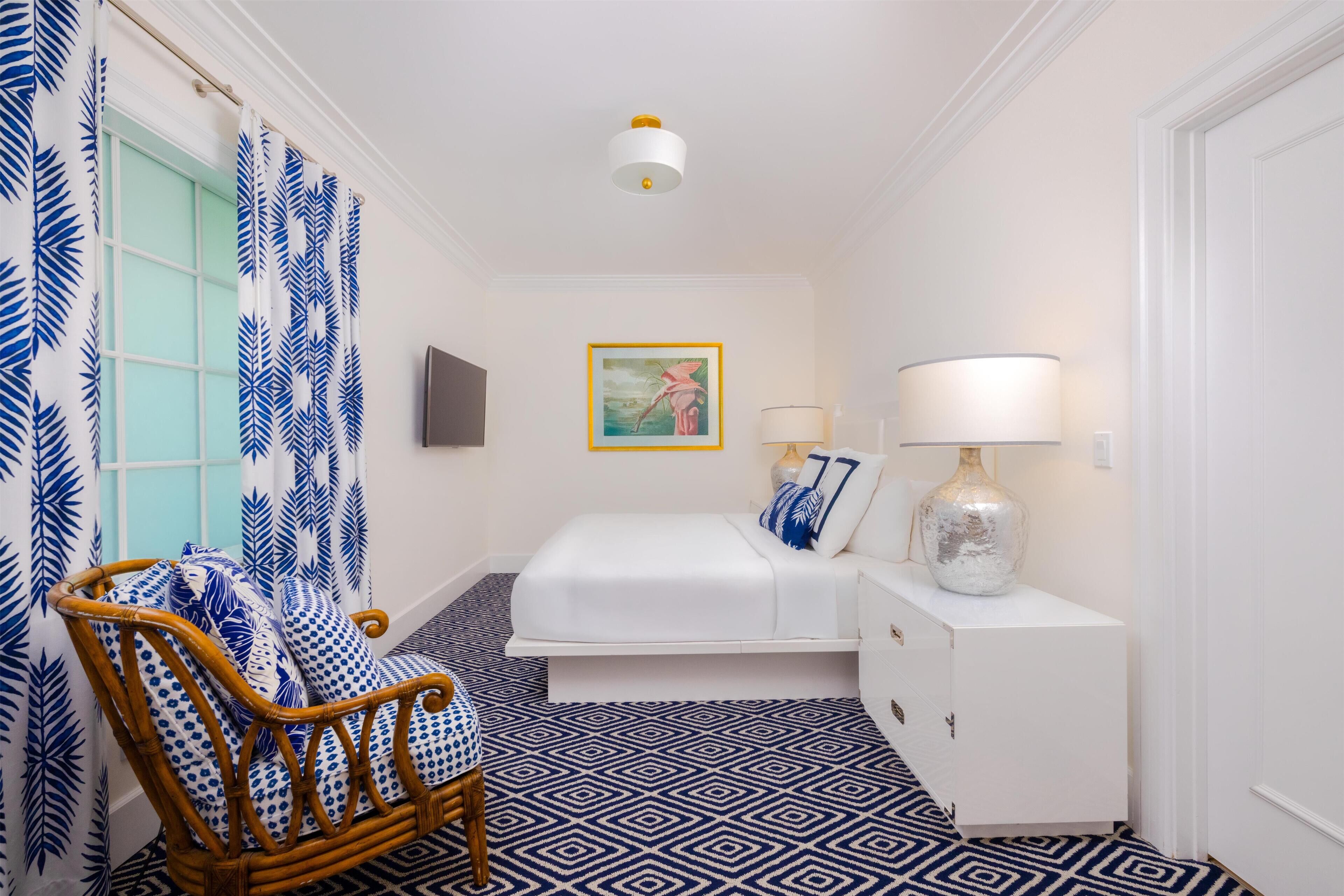 A bedroom with a bed, a bedside table with a lamp, a chair, and a wall-mounted picture.