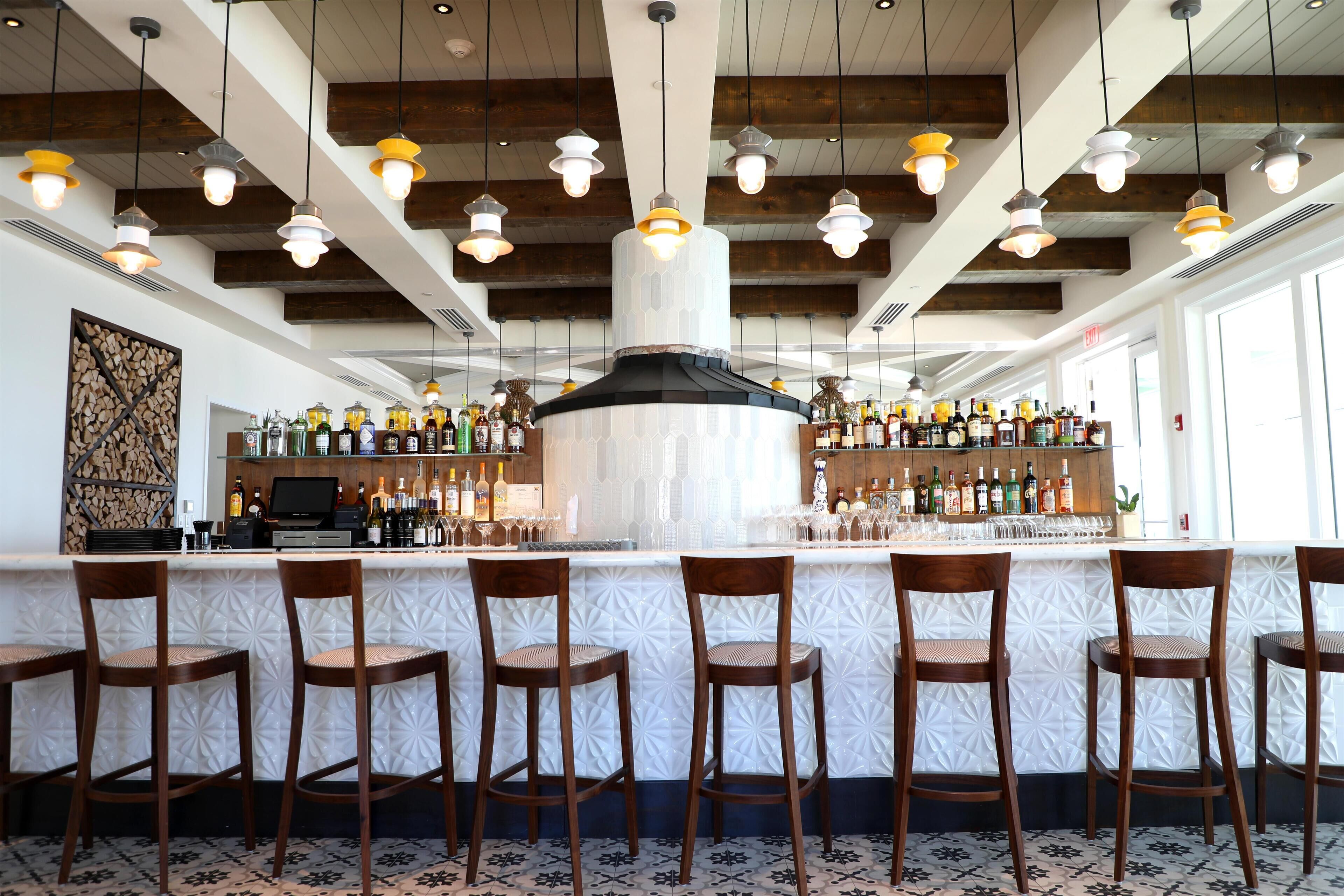 A bar area with wooden bar stools, a central bar counter, and hanging pendant lights.