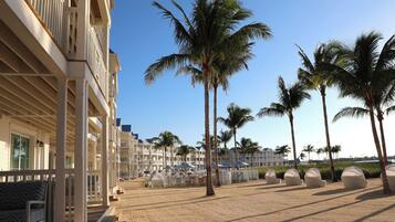 A beachfront hotel with multiple balconies, palm trees, and beach umbrellas.