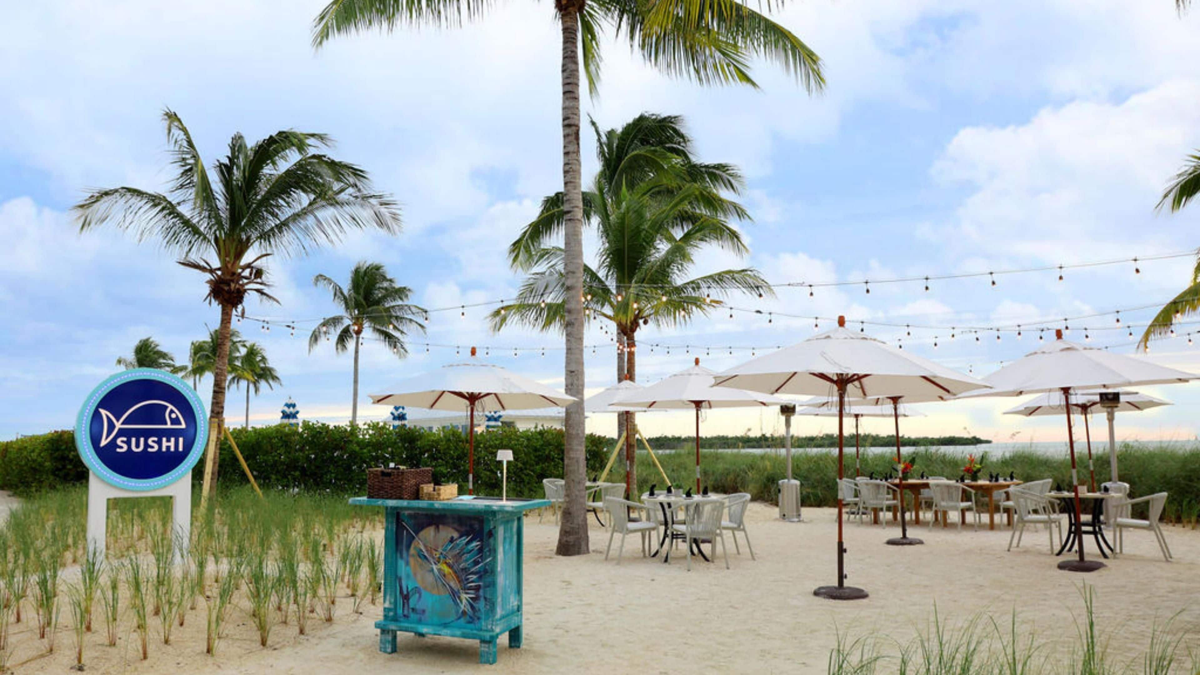 Ein Sushi-Restaurant direkt am Strand mit Außenbestuhlung und Palmen.