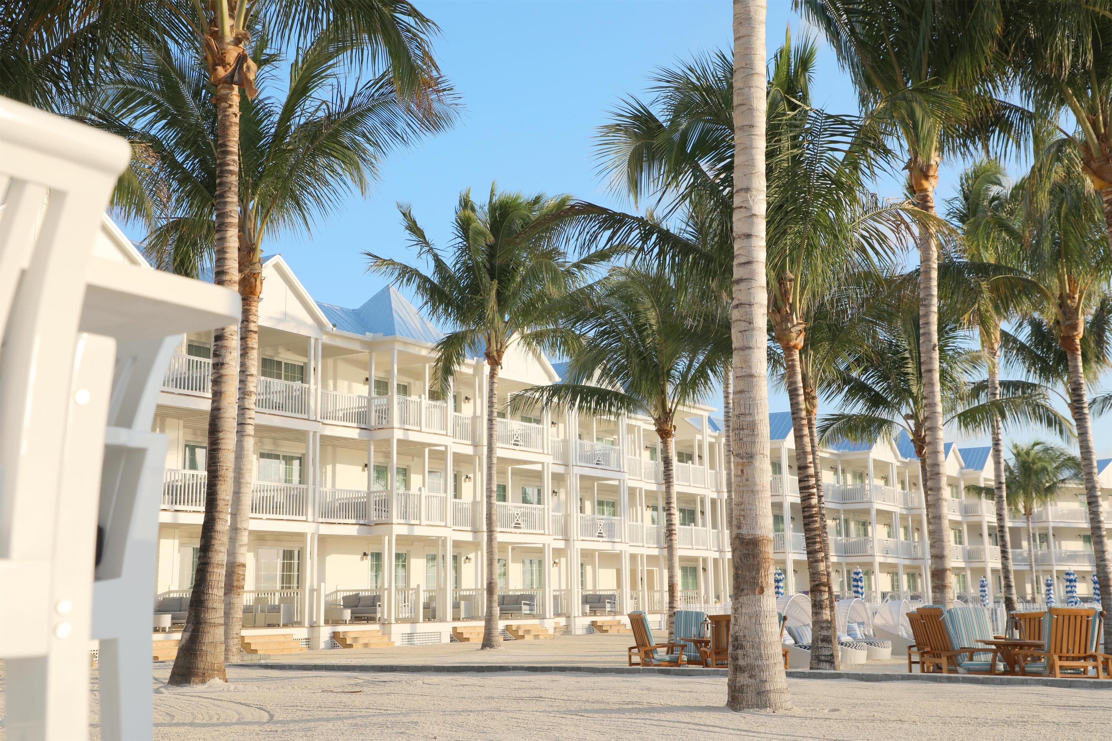 A beachfront hotel with multiple balconies, palm trees, and beach chairs.