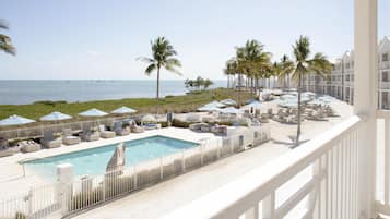 A pool area with lounge chairs and umbrellas, a clear view of the ocean, and a white fence surrounding the pool.