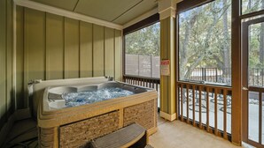 Ein Whirlpool mit einer hölzernen Sitzbank davor, einem Holzwertgang und Blick auf Bäume durch ein großes Fenster.