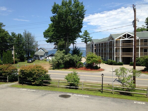 A building with a balcony overlooking a body of water, surrounded by greenery and a clear sky.