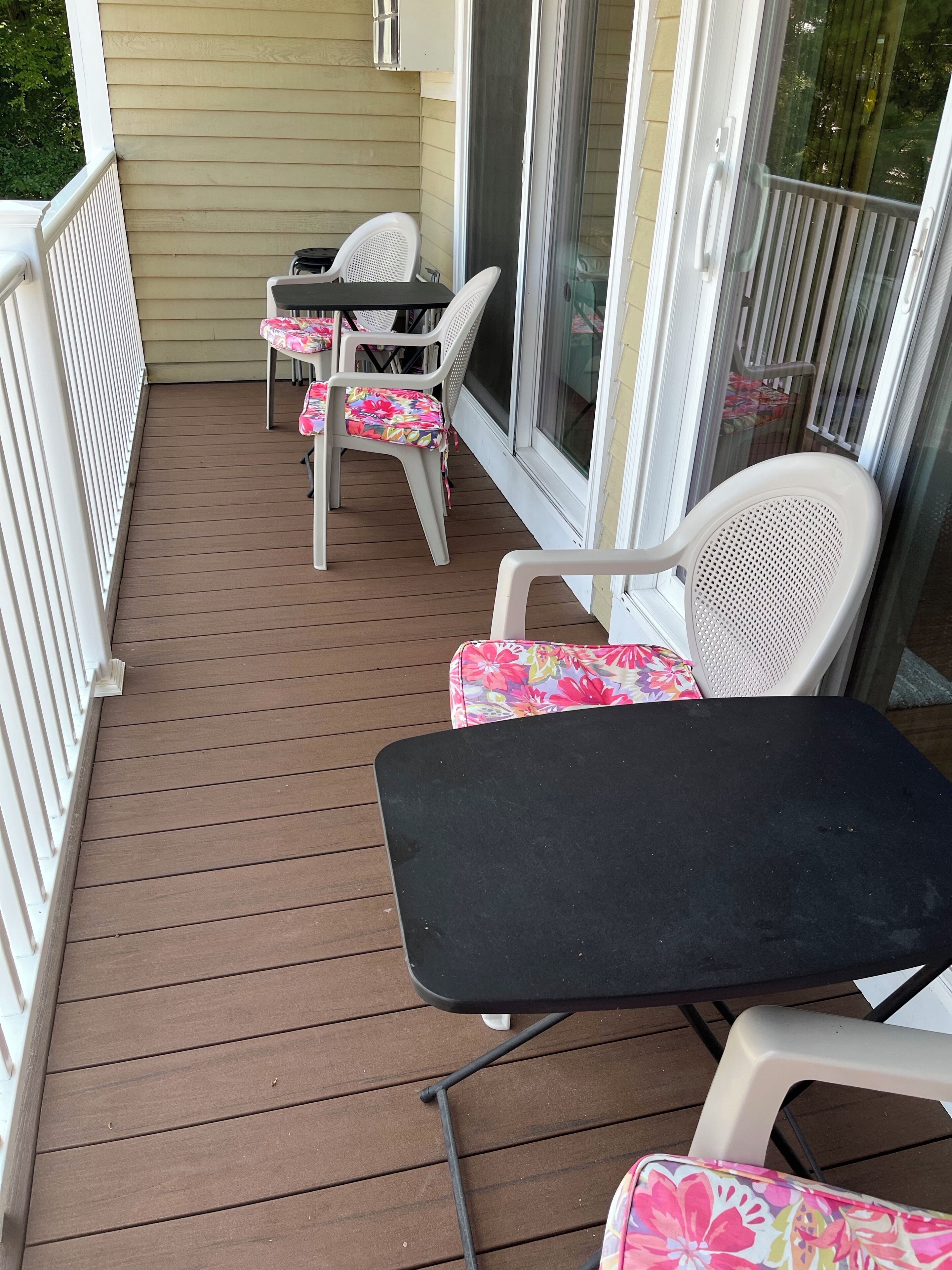 A covered patio with a table and chairs, a sliding glass door, and a white railing.
