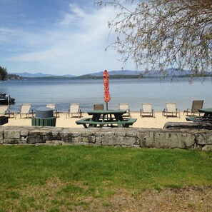 A lakeside picnic area with chairs, tables, and an umbrella.