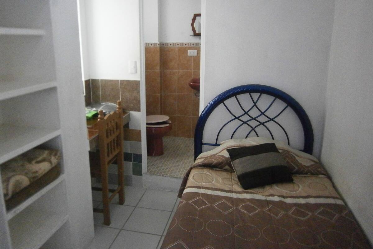 A small, narrow room with a bed, a chair, and a toilet.