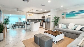 A modern kitchen with a central island, a dining area with a bench, and a living room with a sofa and ottoman.