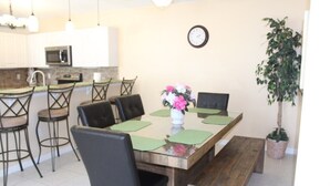 Uma área de refeições com uma mesa de madeira, jogos americanos verdes, cadeiras pretas e um vaso com flores.
