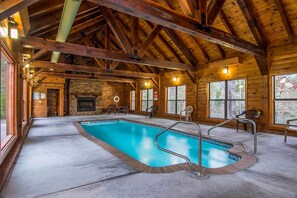 Una cabaña de madera con piscina, chimenea de piedra y grandes ventanales.