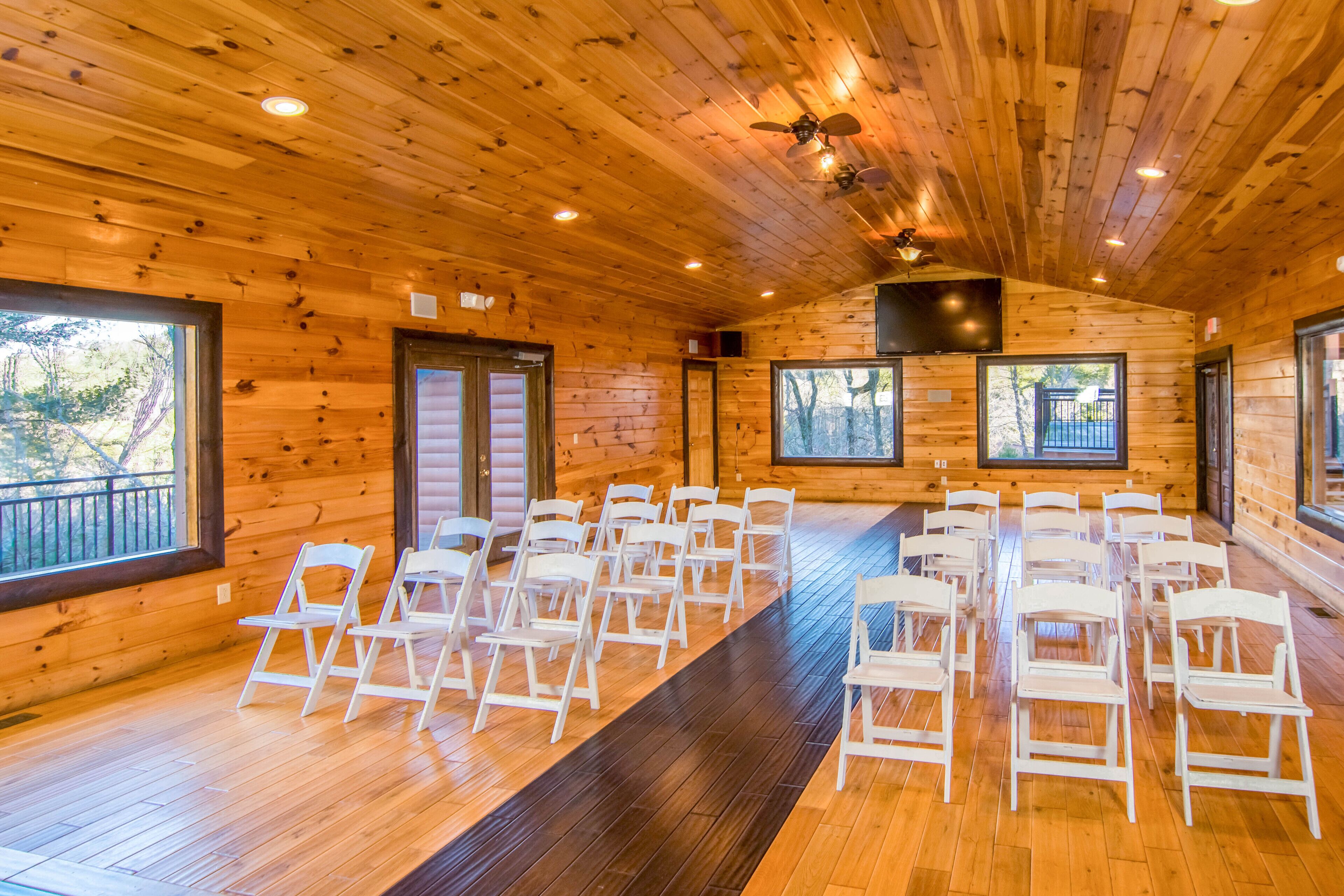 A wooden interior with a long row of white chairs arranged for an event.