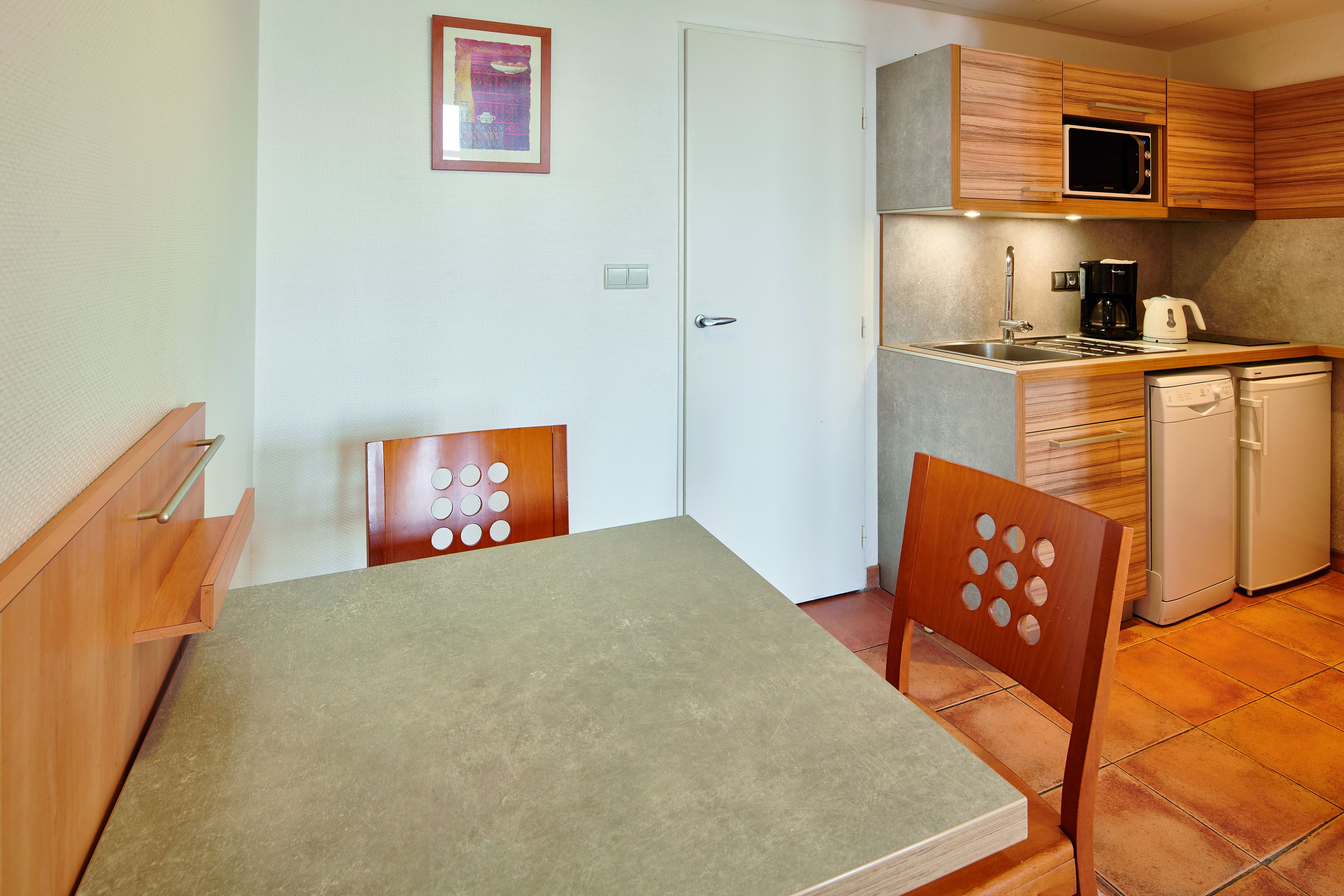 A compact kitchen with wooden cabinets, a microwave, a coffee maker, and a dishwasher.
