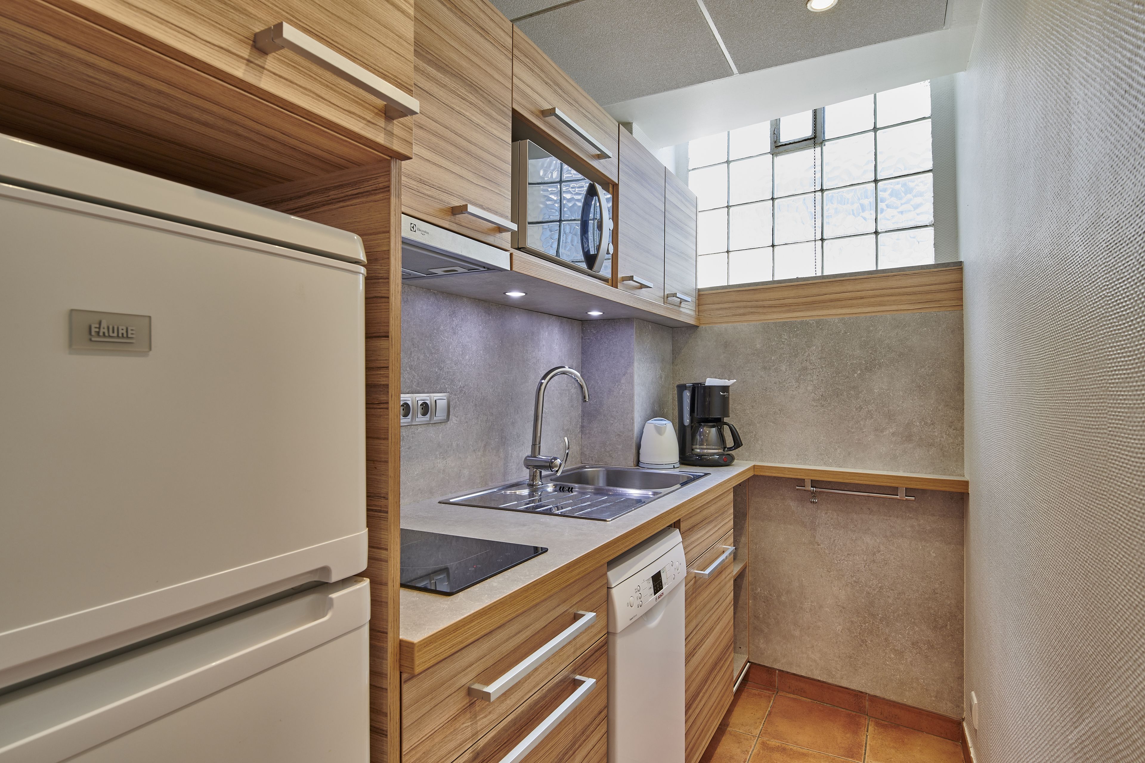 A compact kitchen with a built-in dishwasher, a sink, and a coffee maker.