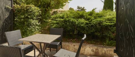 An outdoor patio with a table and chairs, surrounded by greenery and a decorative metal fence.