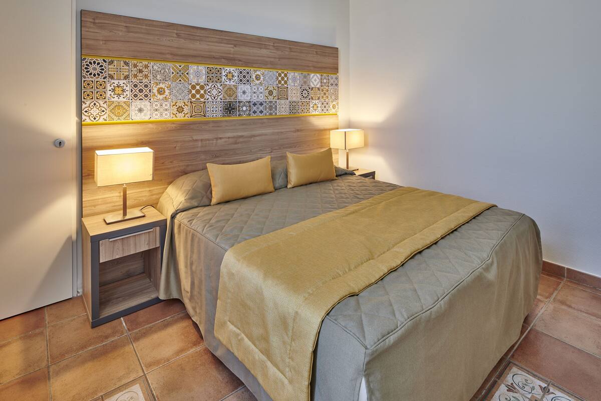 A neatly made bed with a quilted cover and two bedside lamps.