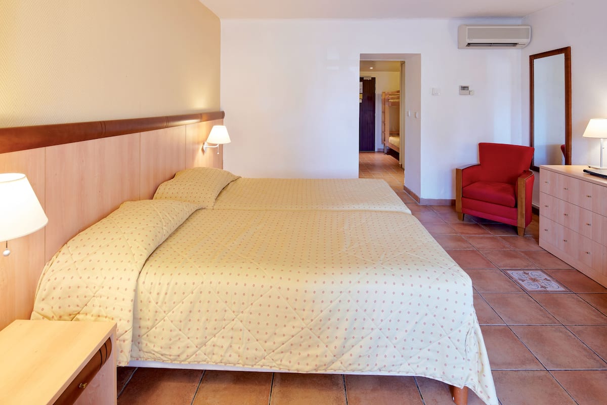 A hotel room with a bed, bedside tables, a chair, a dresser, and an air conditioning unit.