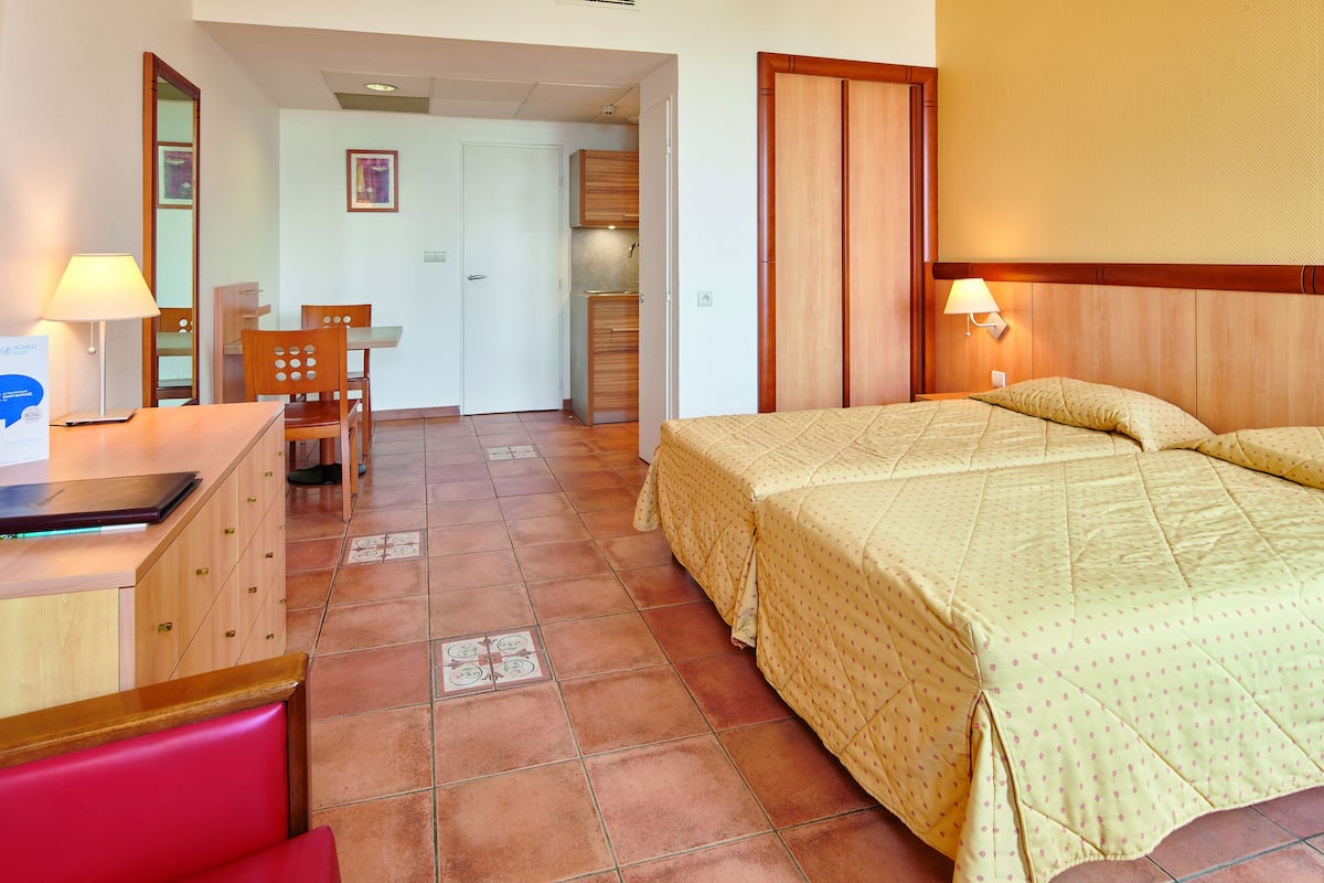 A hotel room with a bed, a desk, a chair, and a small kitchenette.