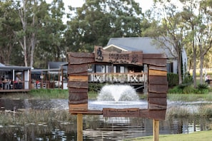 A wooden sign with 'The Deck Café' and 'Lovedale' written on it, placed in front of a building with a water feature behind it.