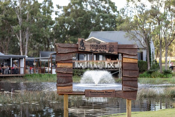 A wooden sign with 'The Deck Café' and 'Lovedale' written on it, placed in front of a building with a water feature behind it.