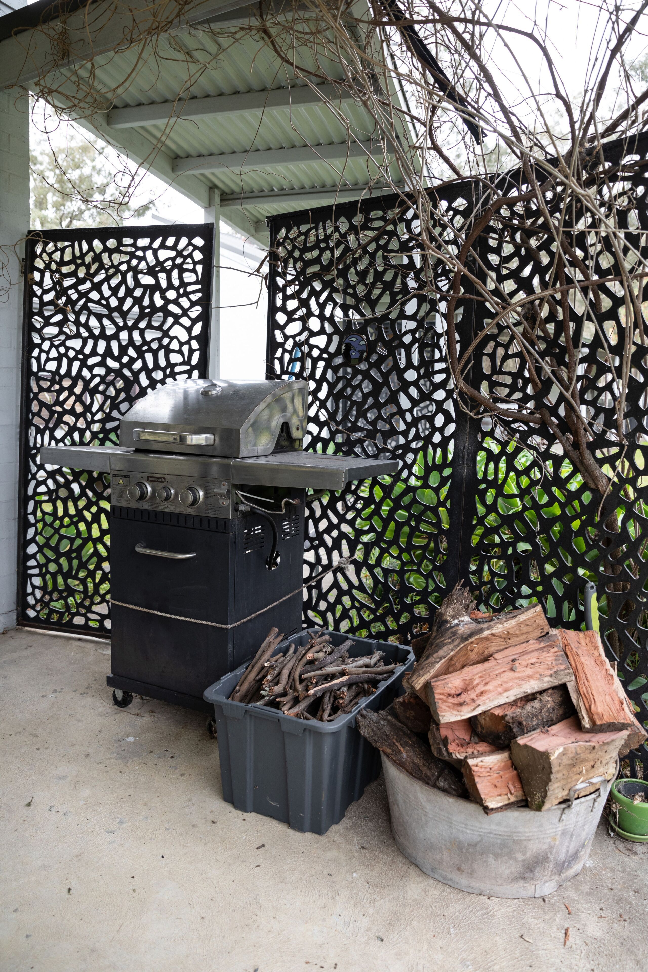 Un barbecue doté d’une grille en métal, d’un récipient contenant du bois et d’une clôture décorative ornée d’un motif géométrique.