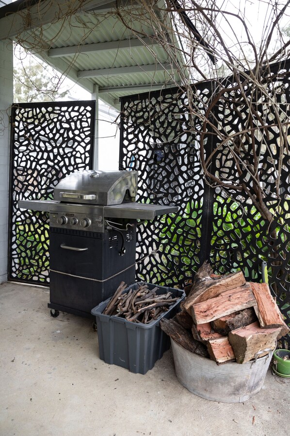 Una parrilla con rejilla metálica, un recipiente de leña y una valla decorativa con diseño geométrico.