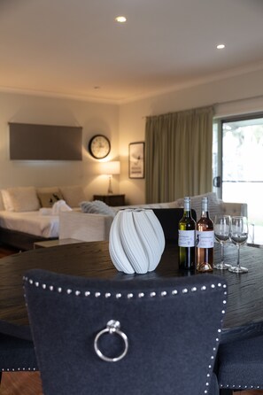 Habitación de hotel con cama, una mesa con botellas de vino y copas, un reloj en la pared y una ventana con cortinas.