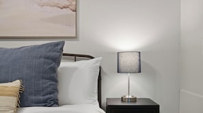 Een bed met een wit en blauw kussen, een lamp op een nachtkastje en een schilderij aan de muur.