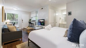 Une chambre d’hôtel moderne équipée d’un lit, d’un canapé, d’un bureau et d’un téléviseur diffusant différentes chaînes.