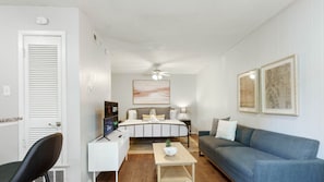 Una sala de estar moderna con una cama, un sofá azul, una mesa de centro blanca y una silla negra.