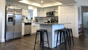 A modern kitchen with a stainless steel refrigerator, a built-in microwave, and a central island with bar stools.