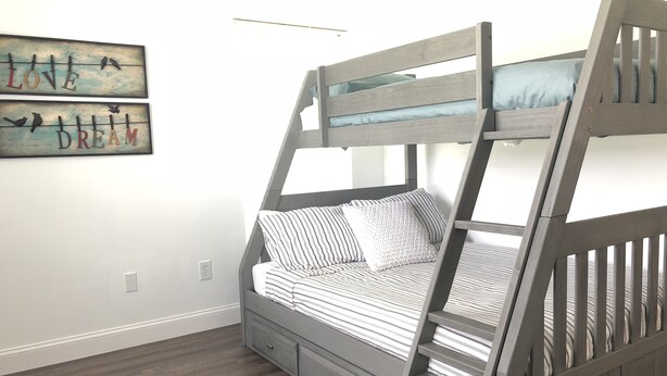 A bunk bed with a wooden frame and drawers, a striped mattress, and pillows. There are two wall decorations with text and birds.