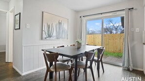 A dining area with a table and chairs, a large window with curtains, and a cactus artwork on the wall. - Kinney #4 xxxxxxxxxx (Austin)