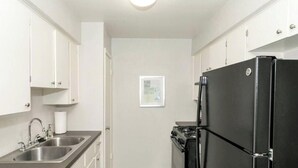 A compact kitchen with white cabinets, a stainless steel sink, a black refrigerator, and a small stove. - Kinney #4 xxxxxxxxxx (Austin)