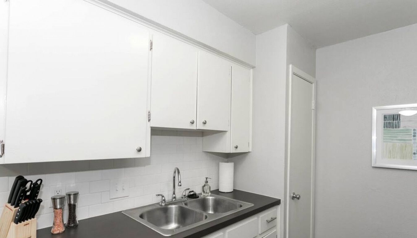 A modern kitchen with white cabinets, a double sink, and a countertop with a knife block and salt and pepper shakers.