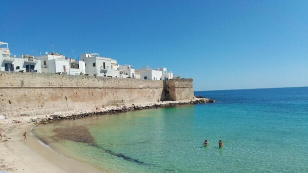 Une ville côtière aux bâtiments blancs, aux eaux turquoise et limpides, et à la plage de sable fin.