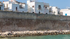 Une ville côtière aux bâtiments blancs, dotée d’un mur de pierre et bordée d’une eau turquoise cristalline.